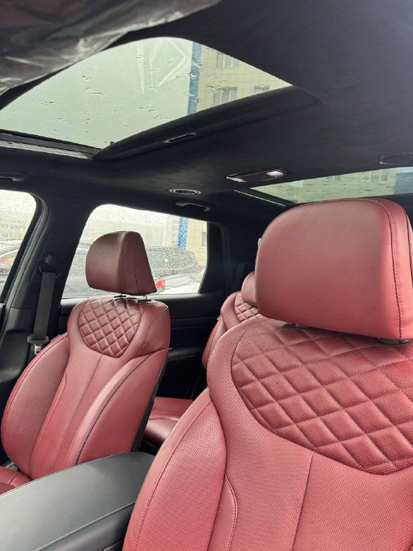 Панорамная крыша и передние сиденья Hyundai Palisade с красной стёганой кожей — вид вверх на люк и интерьер автомобиля при дожде.