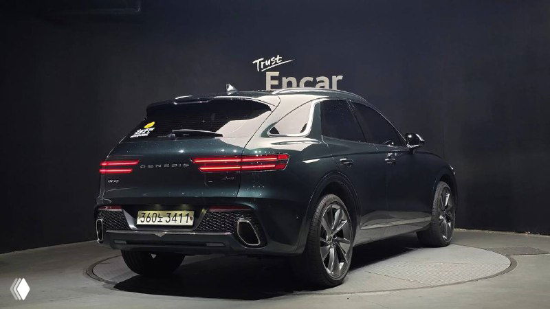 Задний ракурс Genesis GV70 2022 на той же площадке: тёмно-зелёный цвет, вид на фонарь и форму багажника, автомобиль на вращающемся подиуме.