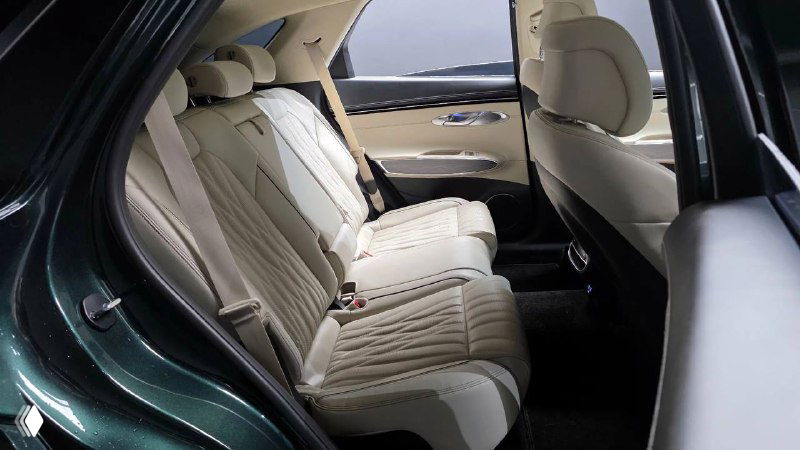 Фото второго ряда сидений Genesis GV70 2022: просторный салон, светлая кожаная обивка и подлокотник, вид на внутренний объем автомобиля.