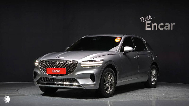 Ещё один внешний вид Genesis GV70 2022, светло-серебристый вариант на подиуме Encar, фронтальный ракурс с видимой решёткой радиатора и бампером.