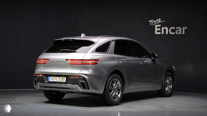 Задняя часть серебристого Genesis GV70 2022: дизайн фонарей, форма багажника и нижняя часть бампера в студийном освещении на площадке.