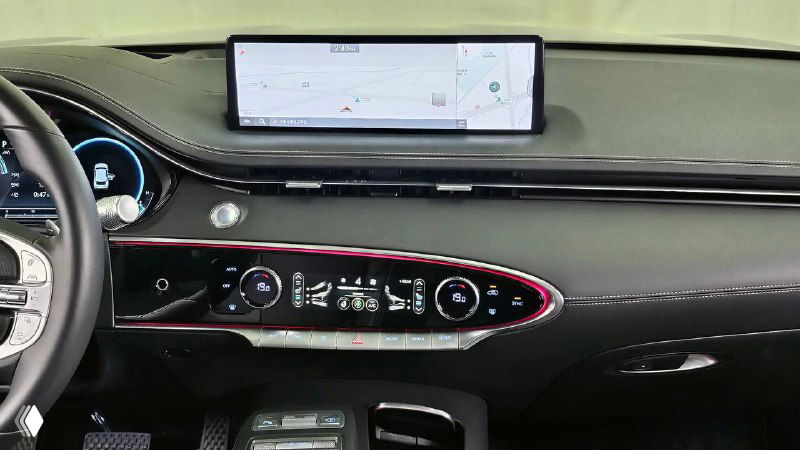 Панорамный вид на приборную панель и навигационный экран Genesis GV70 2022: крупный экран над торпедо и элементы управления на передней панели.