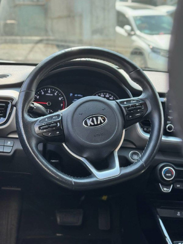 Салон: крупный план рулевого колеса KIA с логотипом, панель приборов и органы управления видны на фоне стекол и улицы