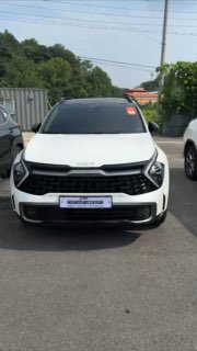 Фронтальный вид белого KIA Sportage 2022 года на стоянке поставщика: видна передняя оптика и решётка радиатора, контекст — автомобиль под заказ/импорт.
