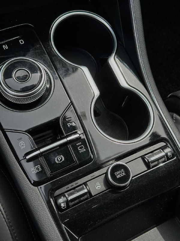 Крупный план центральной консоли KIA K5 с подстаканниками, селектором и органами управления — фото для подтверждения комплектации и функционала.