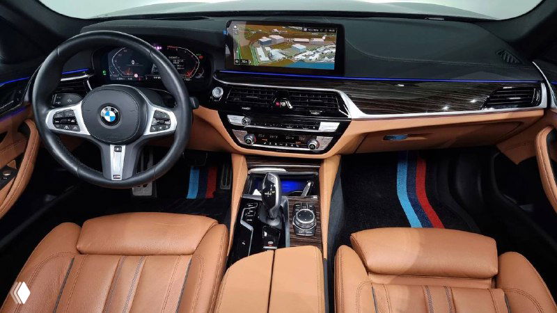 Салон BMW 520i: коричневая кожаная отделка сидений, рулевое колесо и центральная консоль с крупным экраном мультимедиа, вид спереди.