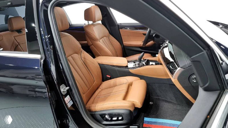 Передние сиденья BMW в коричневой коже, вид через открытую дверцу, видны регулировки сидений и боковые подушки, аккуратная отделка.