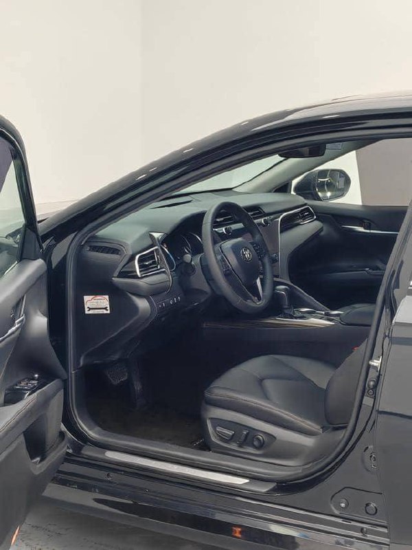 Открытая водительская дверь Toyota Camry 2020, вид на переднее сиденье, порог и настройки кресла; фото показывает состояние обивки и удобства водителя.