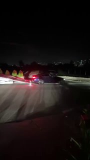 Резкое ночное фото: автомобиль на рампе автовоза во время погрузки, видны фары и отражения на асфальте.