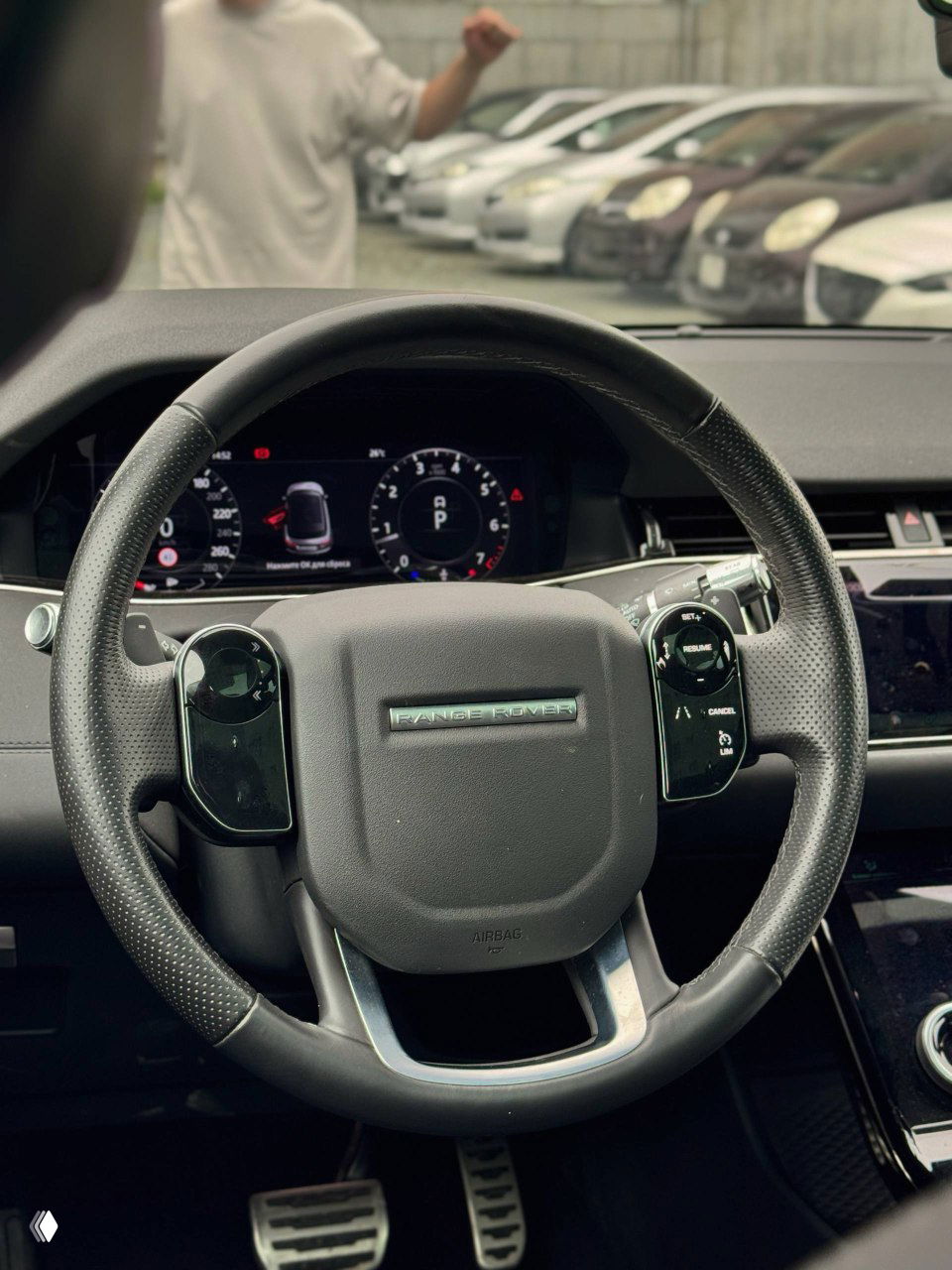 Крупный план рулевого колеса Range Rover Evoque: кожаный руль с логотипом, цифровая приборная панель и часть салона видны с водительского места.