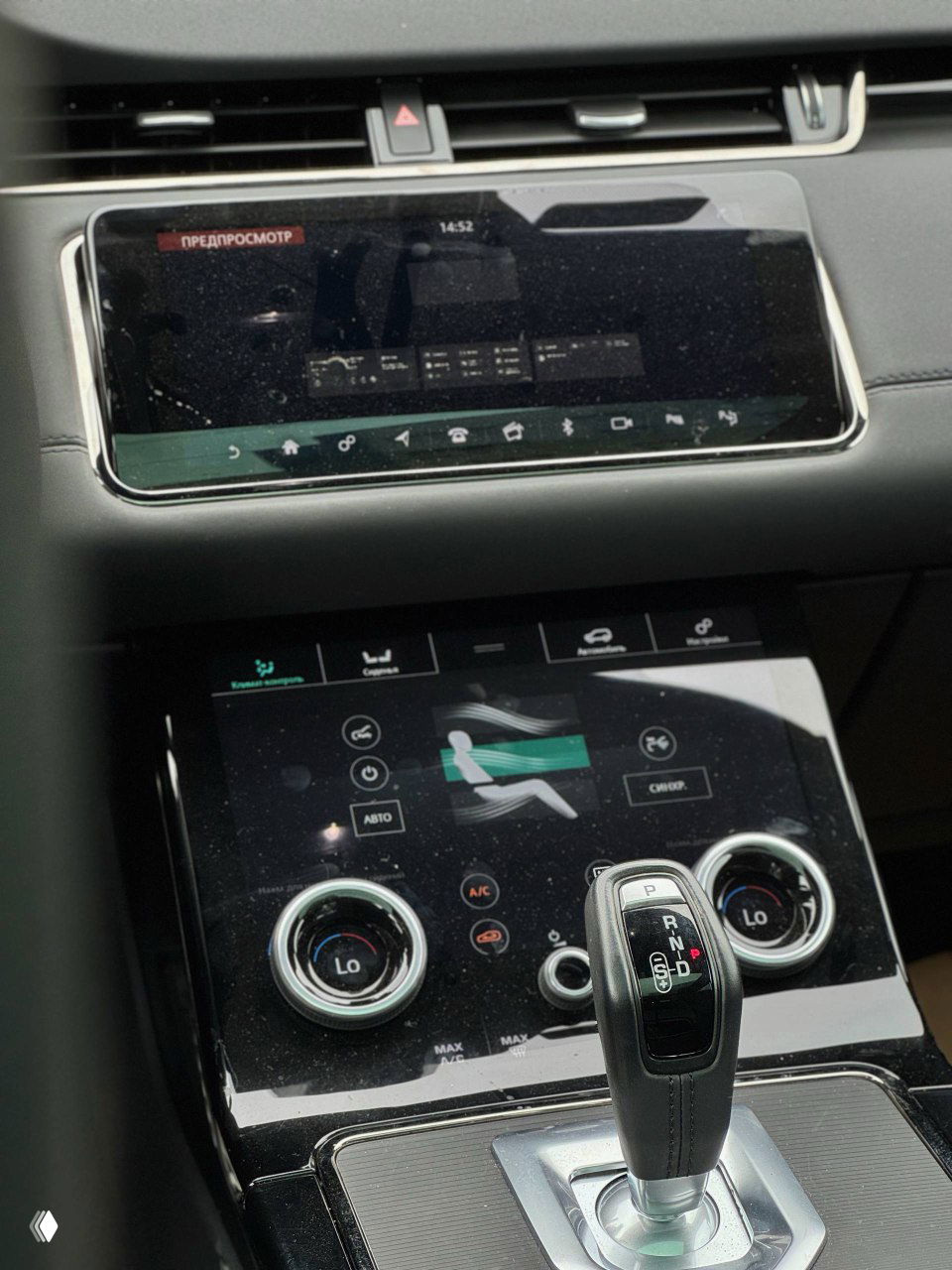 Центральный сенсорный дисплей мультимедийной системы Range Rover Evoque и верхняя панель климат-контроля в глянцевой окантовке крупным планом.