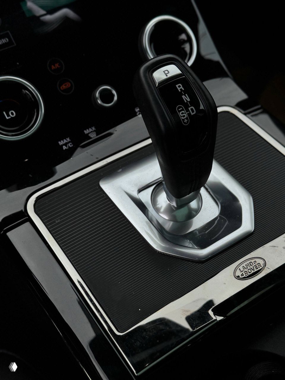 Крупный план селектора коробки передач Range Rover Evoque, чёрный рычаг на центральной консоли с глянцевой отделкой и маркировкой передач.
