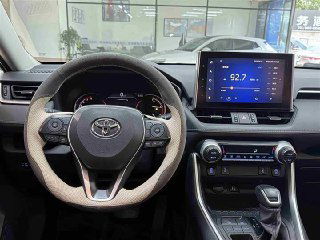 Интерьер Toyota RAV4 2021, вид на приборную панель и экран мультимедиа, салон с кожаной оплёткой руля и центральной консолью.