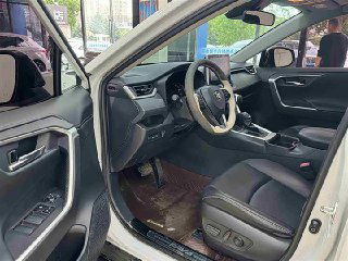 Вид салона Toyota RAV4 2021 с открытой передней дверью: кресла, панель и водительская зона, кожаная обивка и регулировки сиденья.