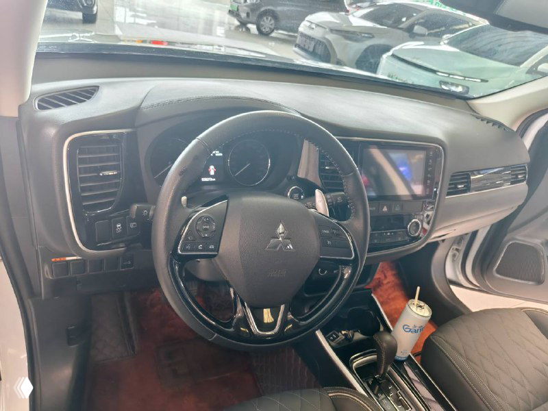 Интерьер Mitsubishi Outlander 2021: рулевое колесо, приборная панель и мультимедийный экран, вид через лобовое стекло на переднюю часть салона.