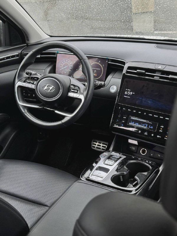 Вид салона Hyundai Tucson — рулевое колесо, цифровая приборная панель и центральная консоль с экраном, аккуратная отделка и эргономика передней части салона.