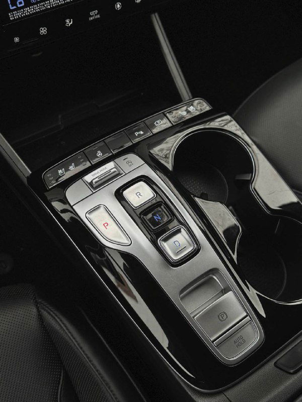 Крупный план селектора коробки передач и пространства между передними сиденьями Hyundai Tucson, видны подстаканники и кнопки управления трансмиссией.