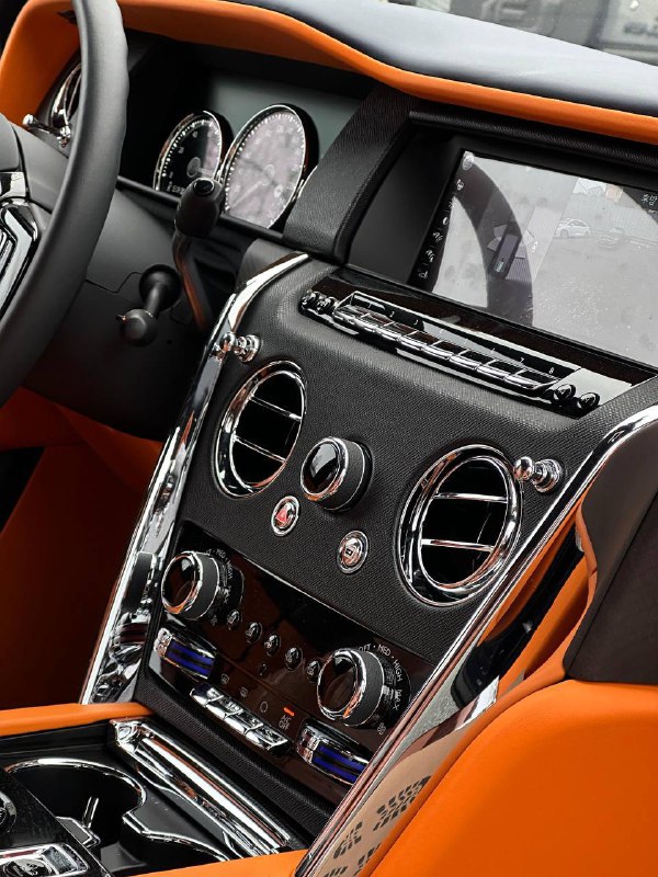 Крупный план центральной части торпеды Cullinan: хромированные элементы, регуляторы климата и контрастная оранжевая кожа на фоне карбона.