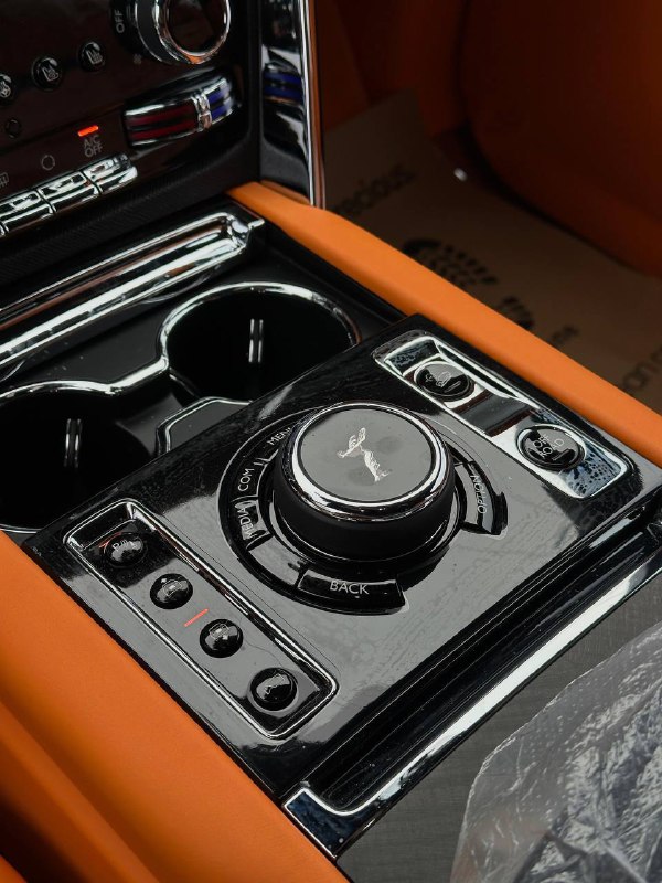 Блок управления на центральной консоли Rolls‑Royce Cullinan: вращающийся контроллер, кнопки, декоративные панели и подстаканники вблизи.
