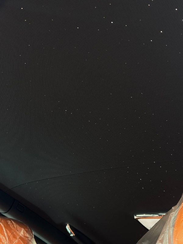 Крупный кадр темной обшивки потолка с небольшими светлыми точками — видна текстура материала и возможные следы или дефекты.