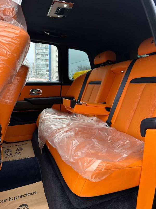 Задний ряд салона Rolls‑Royce Cullinan с яркой оранжевой кожей: два посадочных места, защитная плёнка на сиденьях и общий вид задней зоны.