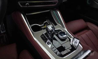 Крупный план центральной консоли BMW X6 xDrive 40i M‑Sport 2021: селектор передач, шайба управления iDrive и декоративные элементы отделки, красная кожа рядом.