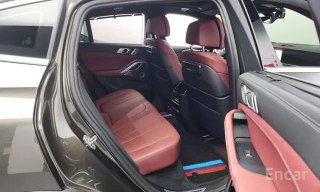 Задний ряд сидений BMW X6 xDrive 40i M‑Sport 2021: красная кожаная обивка, простор для пассажиров, вид сбоку с открытой дверью, чистый и ухоженный салон.