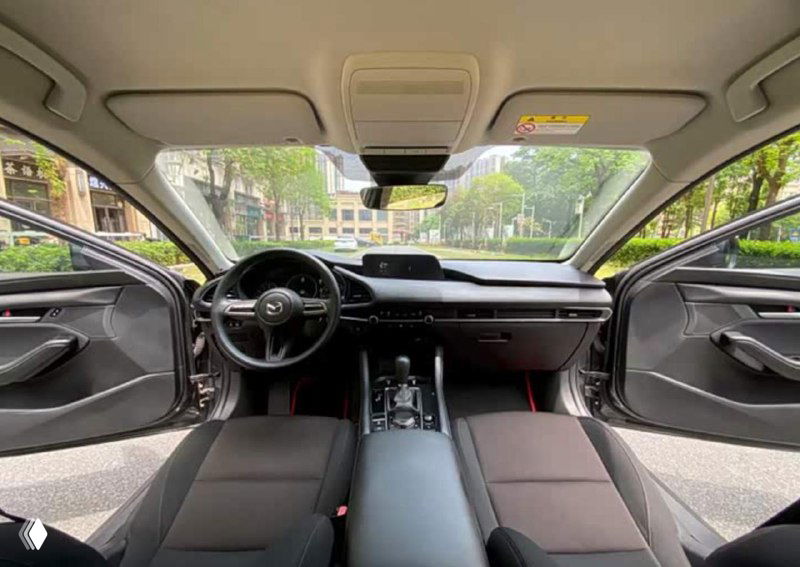 Салон Mazda 3, вид на торпедо и рулевое колесо спереди; показаны приборная панель, центральная консоль и общее состояние отделки для покупателя.