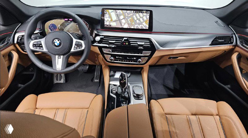 Интерьер BMW 5‑Series: вид на руль, приборную панель и большой мультимедийный экран, коричневая кожаная отделка и элементы отделки салона.