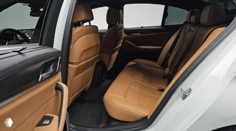 Задний ряд BMW 5‑Series с коричневой кожаной обивкой, пространство для пассажиров и вид на дверную панель и места для ног.
