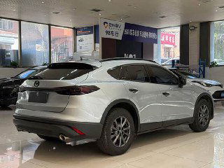 Mazda CX‑4 серого цвета, задний ракурс в шоуруме — видна кормовая часть, бампер, фонари и общий профиль паркетника при наружном освещении.