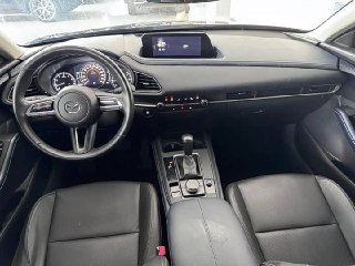 Интерьер Mazda CX-30: вид на рулевое колесо, панель приборов и центральный экран мультимедиа, чёрная отделка сидений и торпедо.