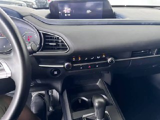Крупный план центральной консоли Mazda CX-30: рычаг КП, органы управления климатом, подстаканники и элементы управления на торпедо в интерьере.