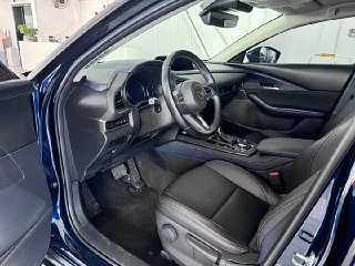 Открытая передняя дверь и водительское место Mazda CX-30: вид на сиденье водителя, дверную обивку и пространство у педалей в реальном салонном окружении.