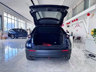 Открытый багажник Mazda CX-30 2020: пустое грузовое пространство, обшивка багажника и задняя дверь в автосалоне на светлом полу.