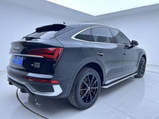 Чёрный Audi Q5L Sportback, ракурс сзади‑сбоку в шоуруме; видна крышка багажника и спортивный профиль кроссовера на светлом фоне.