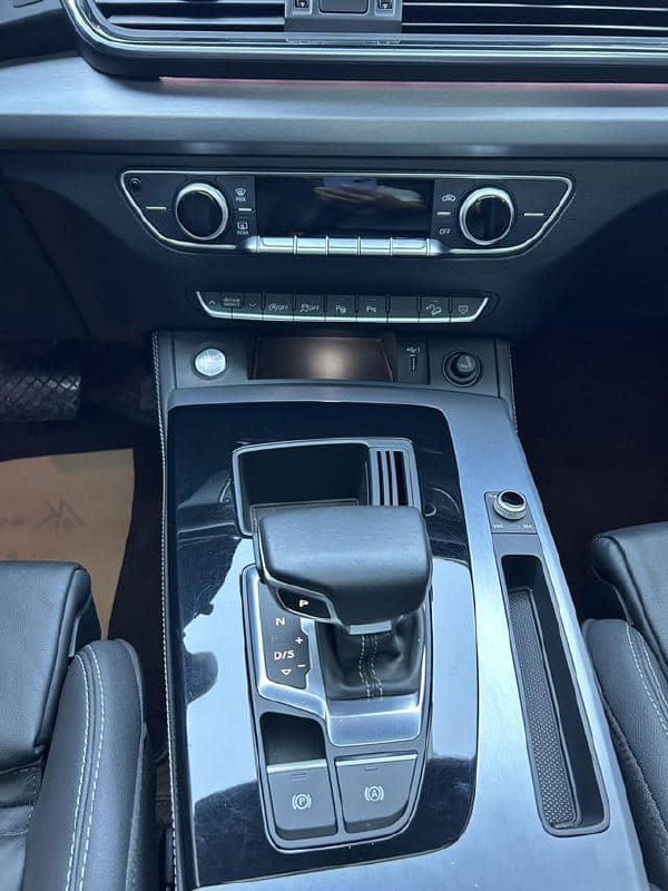 Крупный план центральной консоли Audi Q5L: селектор коробки передач, элементы управления климатом и декоративная глянцевая отделка вокруг рычага.
