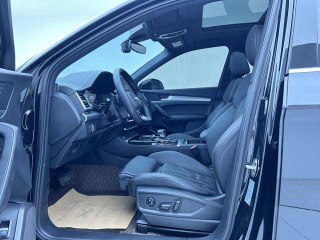 Переднее сиденье водителя и панорамный обзор дверного проёма Audi Q5L, видны регулировки сиденья и чёрная кожа отделки интерьера на светлом фоне.