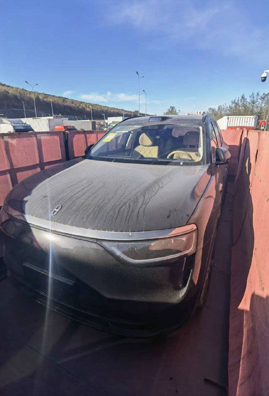 Toyota Highlander 2025 — вид сверху‑переди с солнечным бликом на лобовом стекле, заметен бежевый салон и ограждения контейнера вокруг автомобиля.