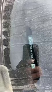 Крупный план лобового стекла с наклейкой VIN и QR‑кодом, видно отражение руки фотографа и цифровую маркировку на поверхности стекла и пыль.