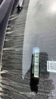 Ракурс на лобовое стекло с штрихкодом и VIN-наклейкой на искривлённой поверхности, чётко видна маркировка и дата съёмки в нижней части кадра.