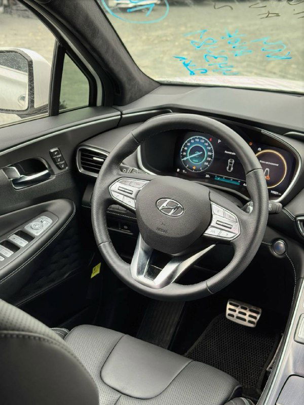 Вид на рулевую колонку и панель приборов Hyundai Santa Fe 2022 — чёрная отделка салона, мультифункциональный руль и цифровая приборная панель, снимок крупным планом.
