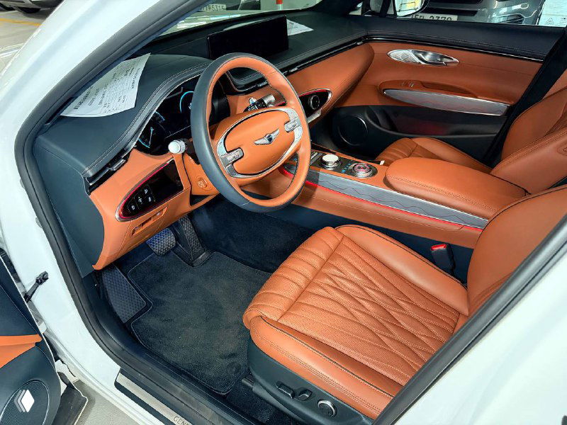 Интерьер Genesis GV70 2023 — передние сиденья в коричневой кожаной отделке, торпеда и рулевое колесо, фото состояния салона для клиента