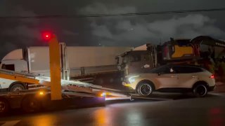 Автомобиль на наклонной аппарели автовоза в ночных условиях, видна часть грузовика и освещение на мокрой дороге во время загрузки.