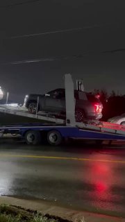 Автовоз на обочине ночью с несколькими автомобилями на нижней и верхней палубах, красные фонари и отражения на мокром асфальте видны отчётливо.