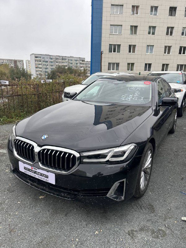 Отдельное фото чёрного BMW на стоянке с наклейкой и отражением зданий на капоте — растаможенный автомобиль.