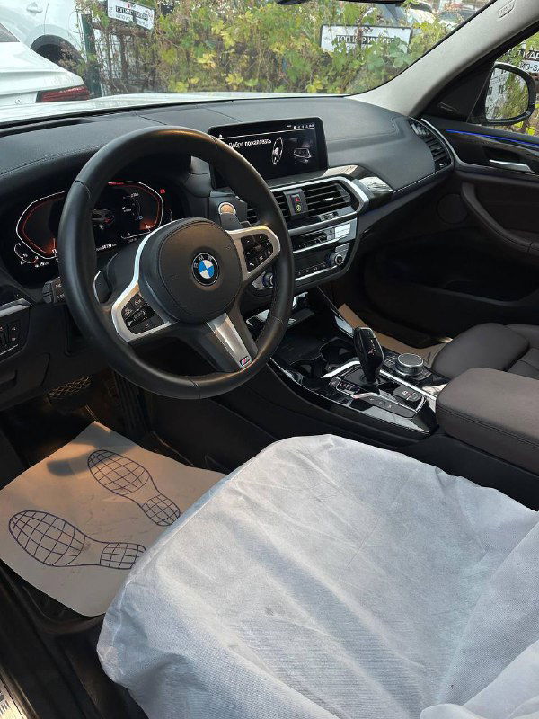 Общий вид передней части салона BMW X3: водительское и пассажирское сиденья, центральный туннель и защитные чехлы на сиденьях.