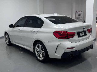 Белый BMW 1‑Series, вид сзади в автосалоне; чётко видны задние фонари, бампер, выхлопная труба и общий профиль багажника и кузова.