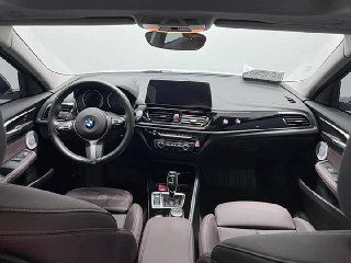 Салон BMW 1‑Series: панель приборов, руль и центральная консоль; фото показывает отделку, мультифункциональный руль и экран мультимедиа.