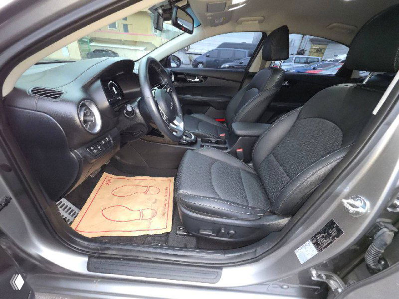 Вид на передние сиденья и водительскую дверь KIA K3 2022: обивка сидений, порог и элементы управления, салон при открытой двери.